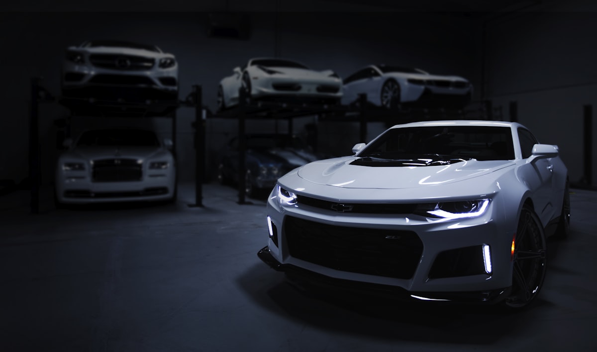 White coupe parked in a garage with other vehicles on lifts